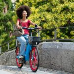 Happy black woman riding electric bicycle on city street bridge